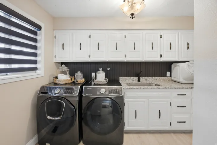 White cabinetry with black hardware, granite-style countertop, and a stainless steel sink with a matte black faucet