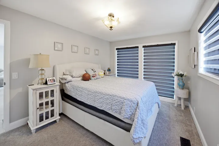 Recessed lighting, light gray walls, light gray carpeting, and multiple windows with layered privacy blinds