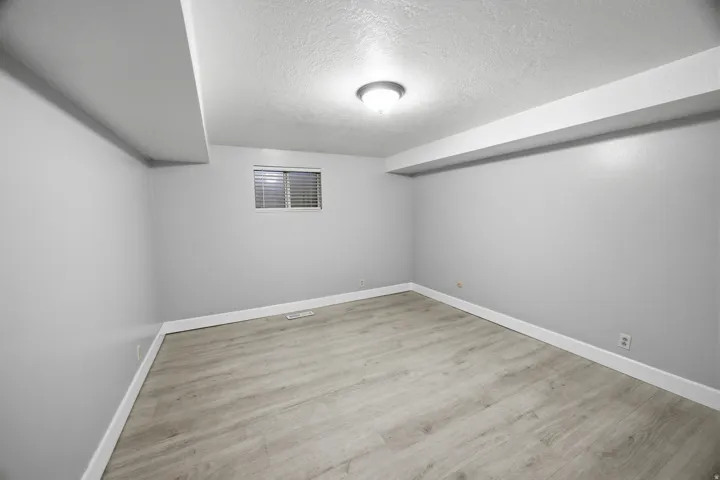 Recessed window with horizontal blinds, overhead flush mount lighting, and wood-finish flooring