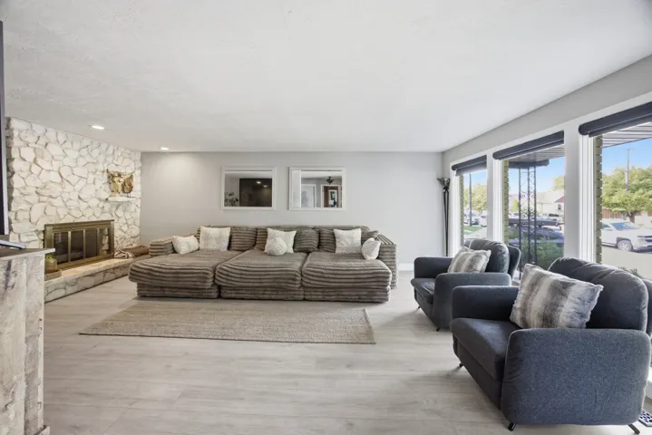 Expansive living area featuring a stone-clad fireplace with a brass-finish insert, large windows, recessed lighting, and wood-finish flooring