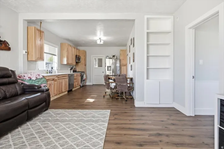 Open concept living area featuring wood-finish flooring, light wood-tone cabinetry, stainless steel appliances, and built-in shelving