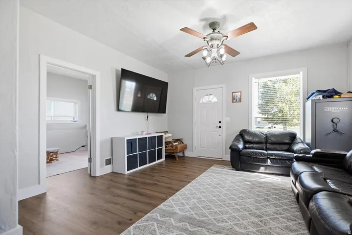 Wood-finish flooring, white paneled door with arched window, and a ceiling fan with integrated lighting