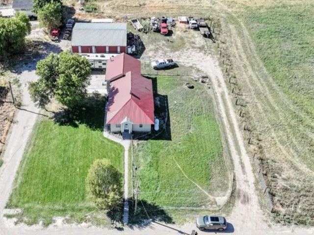 Main structure with red roof, secondary building with red roof, additional outbuilding, expansive grassy area, and surrounding agricultural fields