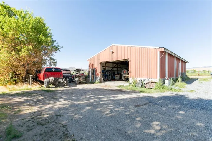 Red metal-sided barn with an open bay door, gravel driveway, and surrounding foliage