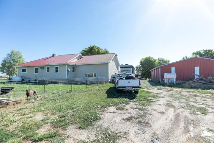 Expansive property featuring a residence with a red metal roof and light-colored siding, a detached red utility building, and a gravel driveway