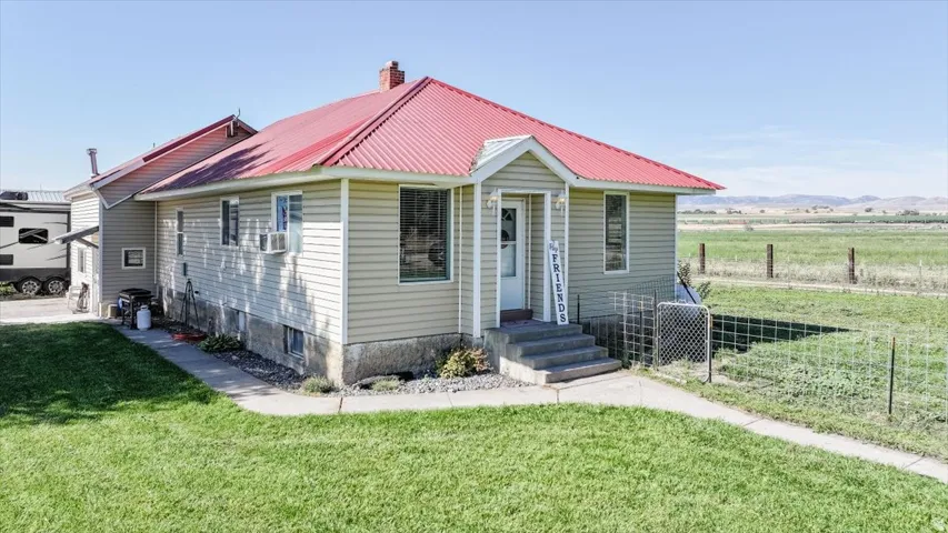 Light-colored siding exterior with a red metal roof and a concrete walkway