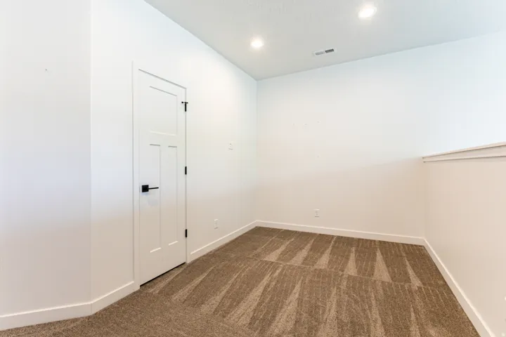 Recessed lighting illuminates a carpeted room with a white panel door and black hardware
