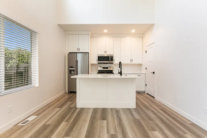 Kitchen featuring white shaker cabinetry, stainless steel appliances, a center island with a white countertop, and wood-finish flooring