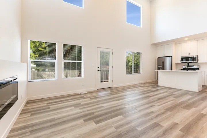 Vaulted ceilings with high windows, wood-finish flooring, white cabinetry, stainless steel appliances, and a kitchen island