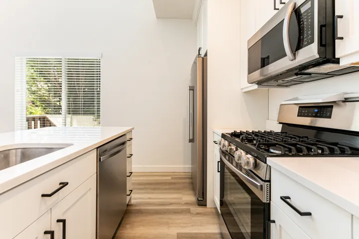 White cabinetry with matte black hardware, stainless steel appliances, light-toned wood-finish flooring, and a stainless steel sink with a white countertop