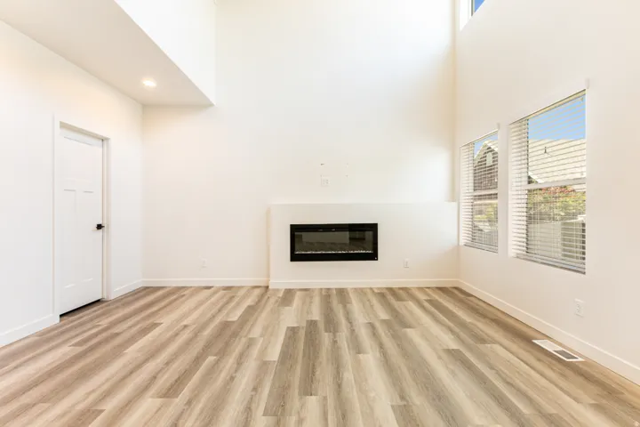 Spacious room featuring vaulted ceilings, wood-finish flooring, an integrated linear fireplace, and multiple windows