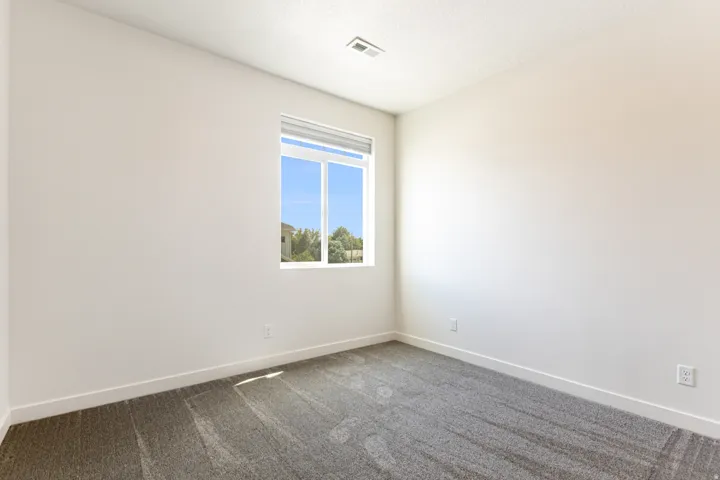 Neutral tone wall paint, textured ceiling, gray patterned carpet, and a window with a roller shade