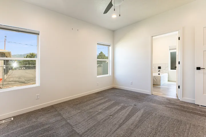 Plush carpeted flooring, a ceiling fan with integrated lighting, and white walls with trim