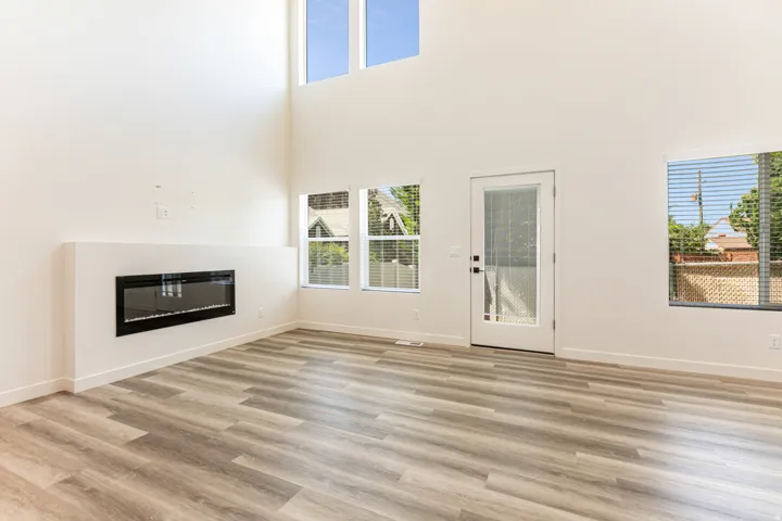 Wood-finish flooring throughout, high ceilings, integrated fireplace, multiple windows, and a glass-paneled exterior door