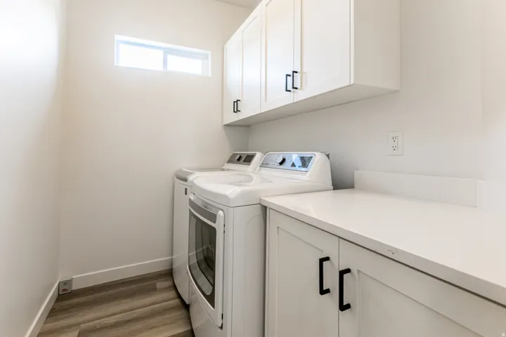 White shaker-style cabinetry with black hardware, white countertops, and wood-finish flooring