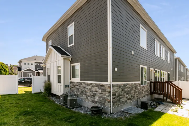 Exterior featuring horizontal siding, stone veneer accents, multiple windows, a rear deck with steps, and white privacy fencing