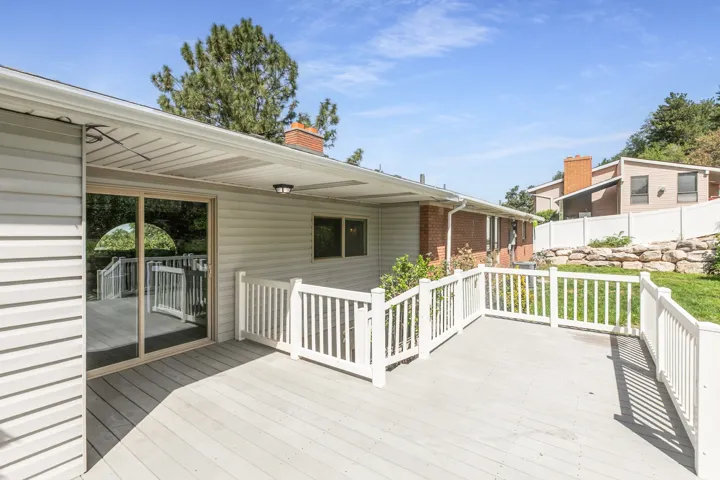 Expansive outdoor deck featuring white railing, sliding glass door access, and a covered patio area