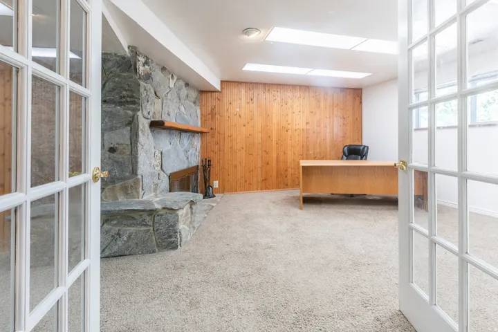 Stone-clad fireplace with wood mantel, wood-paneled accent wall, and french doors with glass panels