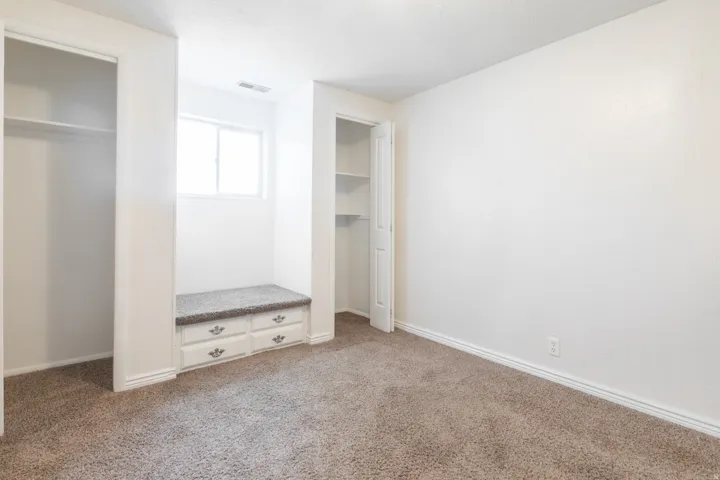Built-in window bench with drawers, two clothing closets with shelving, and carpeted flooring