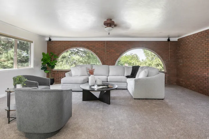 Expansive living area with brick accent wall, arched windows, and a ceiling fan
