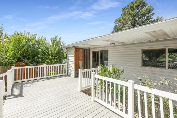 Spacious outdoor deck with painted wood-finish flooring and white railing, sliding glass door access, and vinyl siding exterior