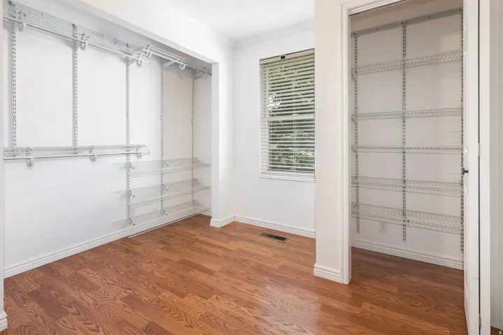 Wood-finish flooring, adjustable wire shelving systems, white trim, and a window with blinds
