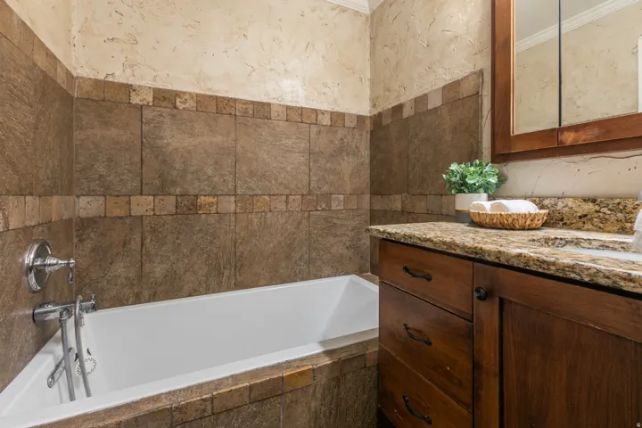 Built-in bathtub with chrome fixtures, tiled surround, and textured wall finish