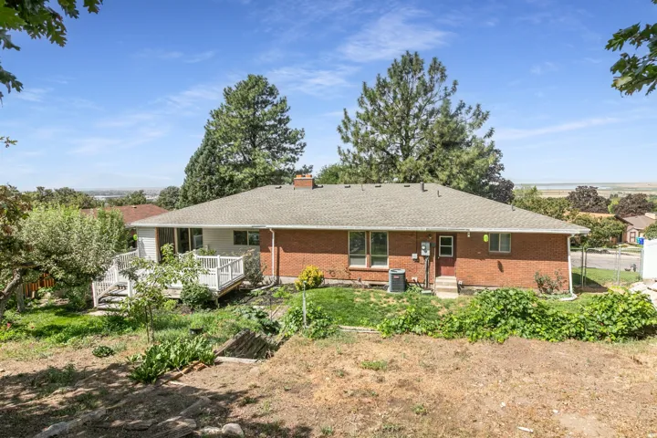 Brick exterior home with a gabled roof, white deck, and mature trees
