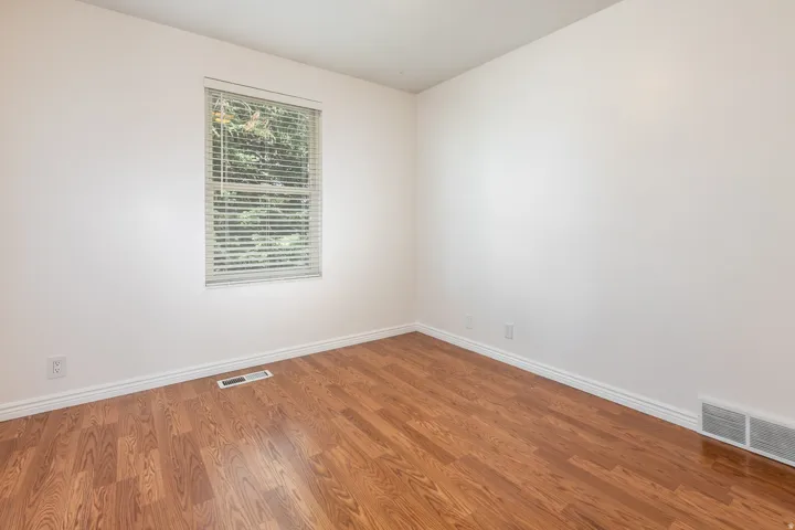 Bright interior with wood-finish flooring, crisp white walls, and a window with horizontal blinds
