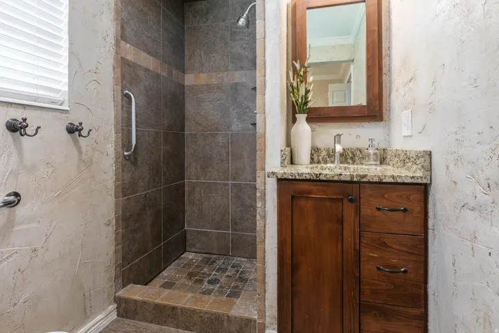 Walk-in shower with tiled walls and floor, wood vanity with granite countertop, and a framed mirror