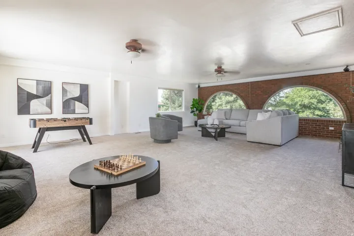Expansive room featuring light-colored carpeting, white painted walls, and an exposed brick accent wall