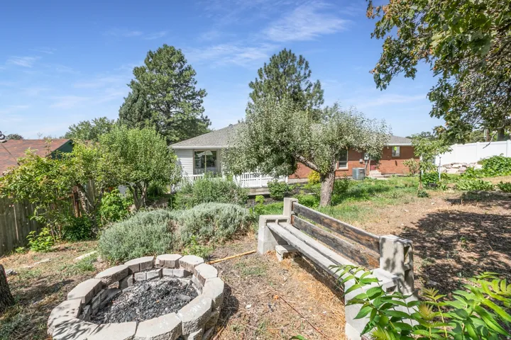 Rear exterior with a stone fire pit, wood and concrete bench, and mature landscaping