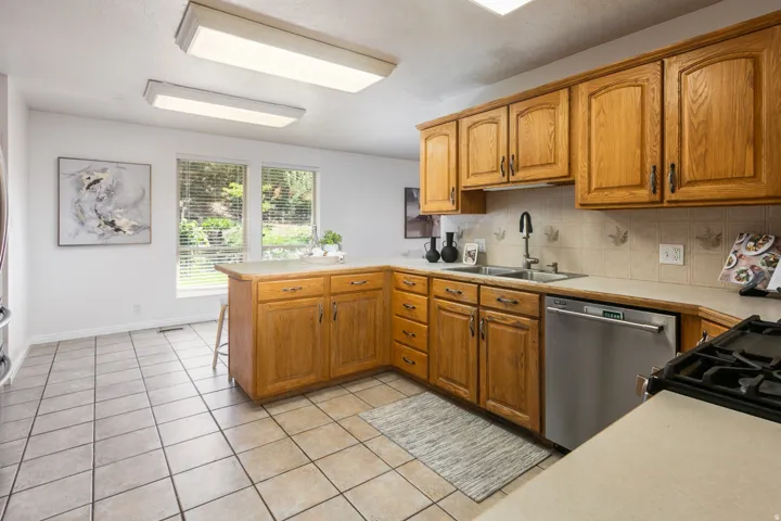 Tile flooring, ample wood cabinetry, dual basin sink, stainless steel dishwasher, and a gas cooktop