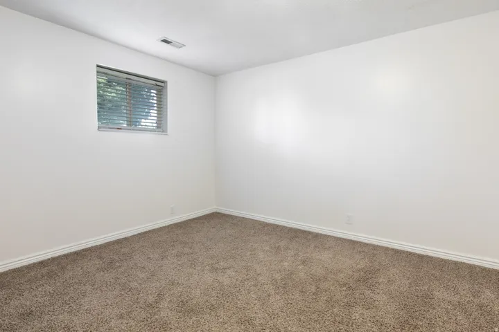 Carpeted room with white walls and a window featuring horizontal blinds