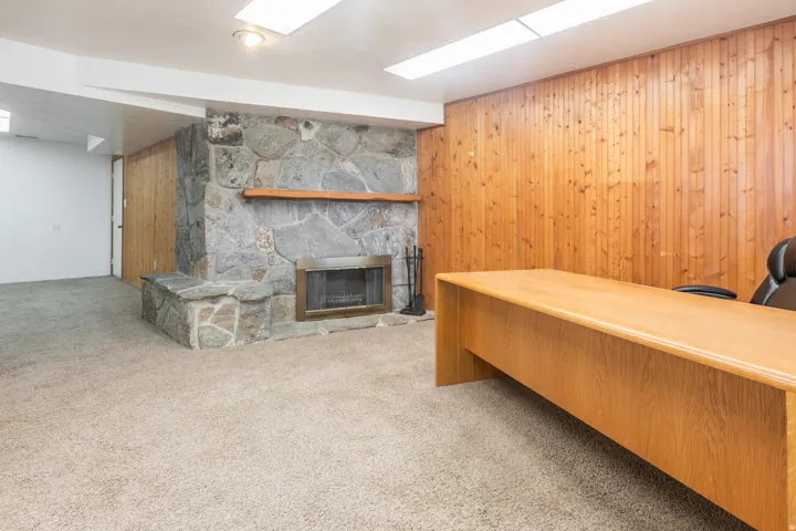 Stone-clad fireplace with a wood mantle, wood paneling, and wall-to-wall carpeting