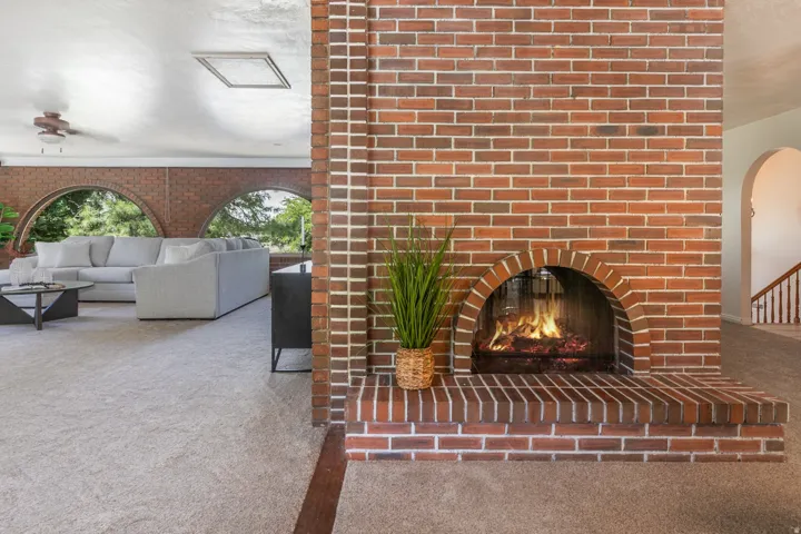 Brick fireplace with an arched opening, integrated brick hearth, and light-toned carpeting