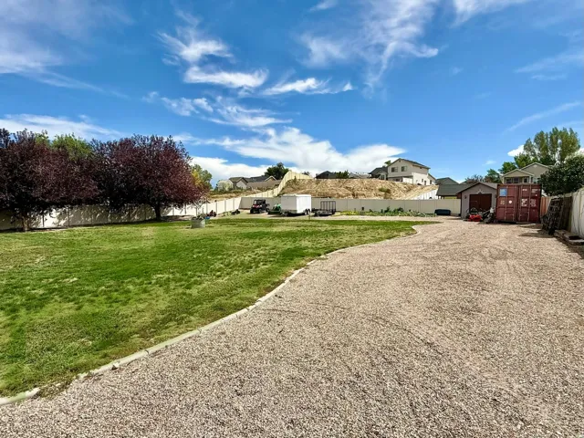 Expansive gravel area, manicured lawn, perimeter fencing, and mature trees