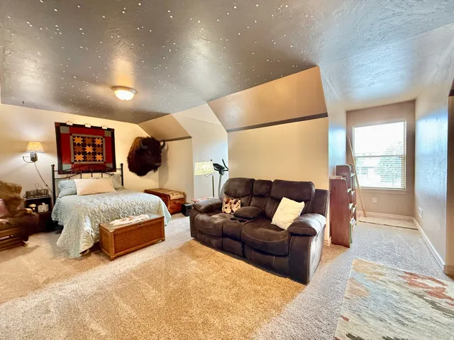 Carpeted room featuring a window with blinds, sloped ceilings, and wall-mounted lighting fixtures