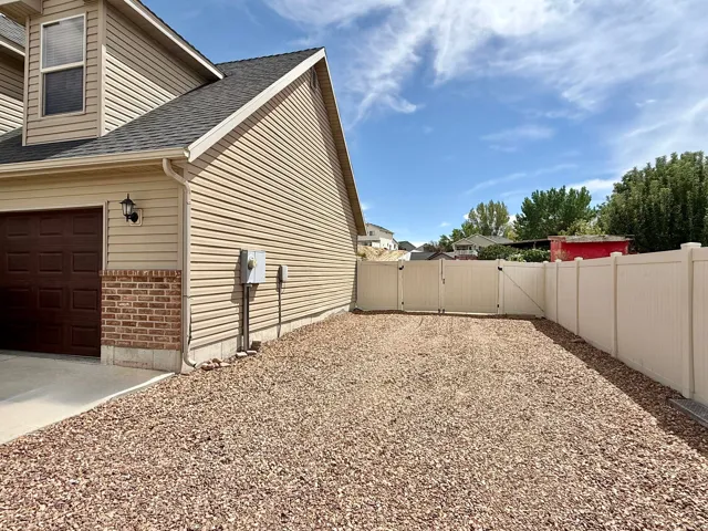 Gravel area with a full vinyl fence and double gates, complemented by a siding and brick exterior