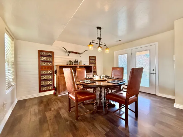 Wood-finish flooring, white shiplap accent wall, built-in wooden cabinetry, double French doors with frosted glass, and a multi-bulb chandelier