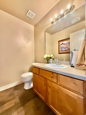 Wood-finish flooring, light wood cabinetry with dark hardware, an integrated vanity sink, and a multi-bulb vanity light fixture