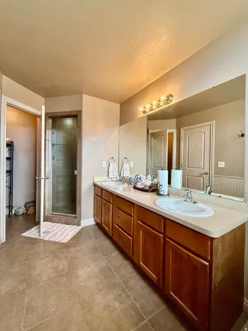 Dual vanity with integrated sinks, extensive countertop space, wood-finish cabinetry, a large mirror, and a glass-enclosed shower