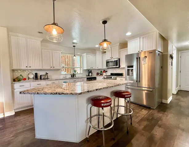 Expansive kitchen island with a granite countertop, white cabinetry with dark hardware, stainless steel appliances, and wood-finish flooring