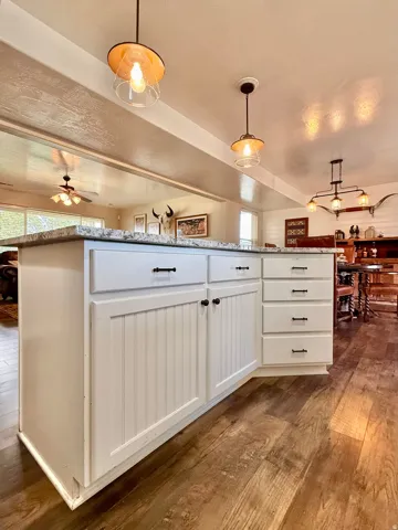 Central kitchen island with white cabinetry and dark hardware, wood-finish flooring, and recessed ceiling lighting