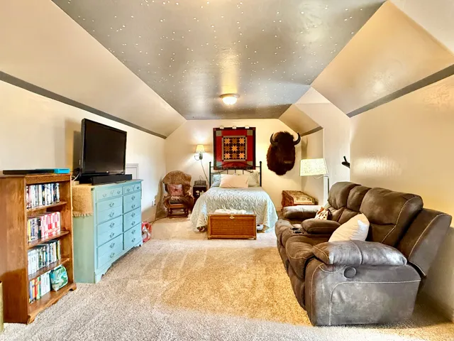 Vaulted ceiling with a unique finish, carpeted flooring, and wall-mounted sconces