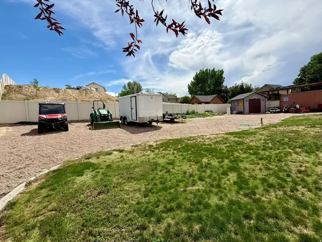 Expansive gravel pad, attached shed with garage door, partial vinyl fencing, and grass area