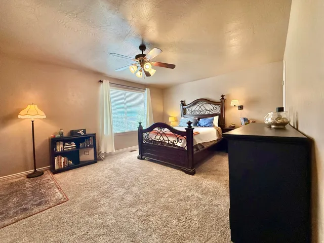Textured wall finish, ceiling fan with integrated lighting, window with blinds and drapes, wall-mounted sconce