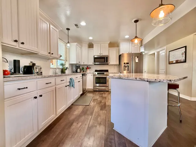Kitchen featuring white shaker and beadboard cabinetry, stainless steel appliances, wood-finish flooring, a white tile backsplash, and a central island with a stone countertop