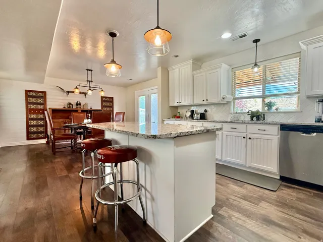 Kitchen featuring an island with stone countertops, white shaker cabinetry, stainless steel appliances, a white tile backsplash, and wood-finish flooring