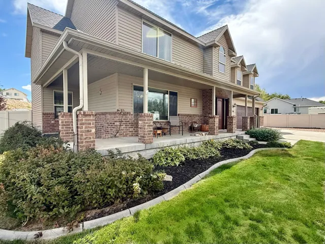 Expansive covered front porch with brick accents, multi-level vinyl siding, dormer windows, and attached garage